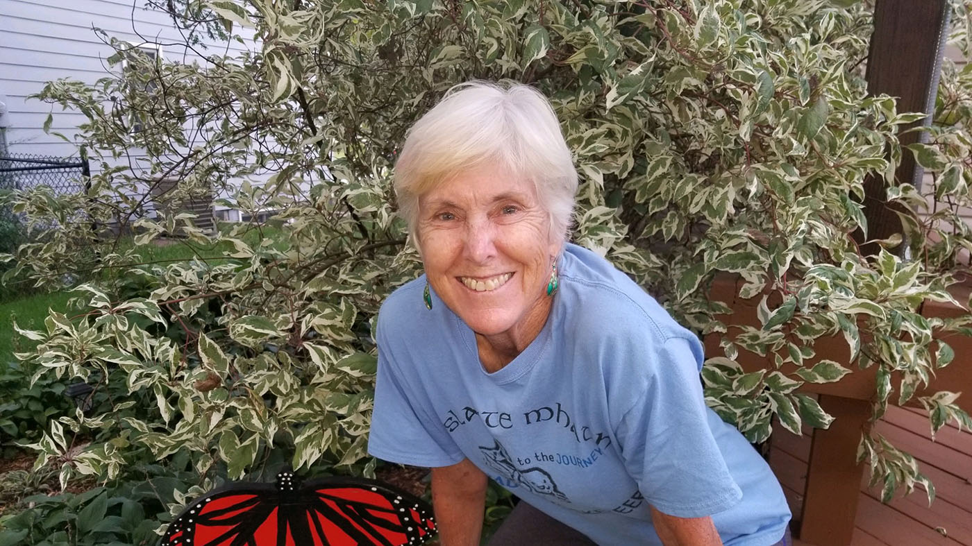 Class of '77 alum Sarah Sebring Binder stands in front of a bush in her garden.
